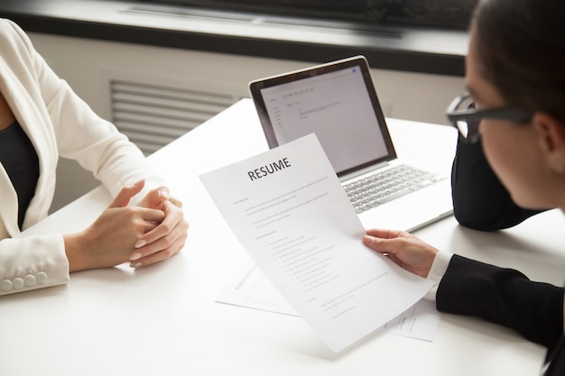 Two people at a desk, one reviewing a resume labeled "RESUME", during a job interview.